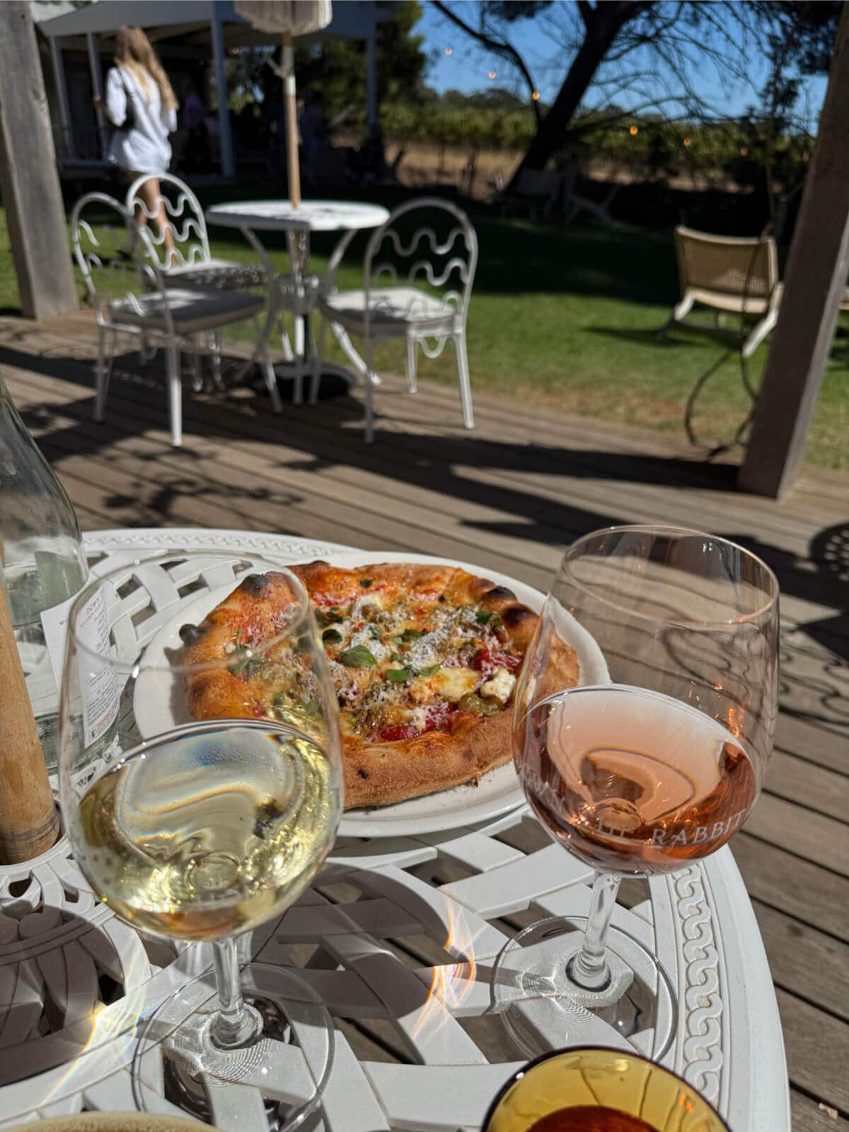 A pizza and glasses of white wine and rose a top a garden table at Down The Rabbit Hole's Cellar Door
