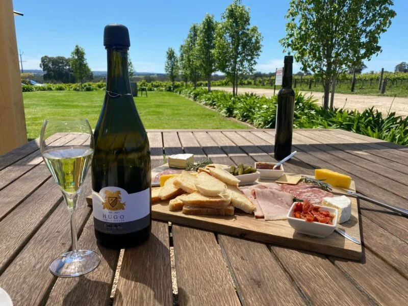 Bottle of wine and food platter, with Hugo Cellar Door's lawn and trees in background