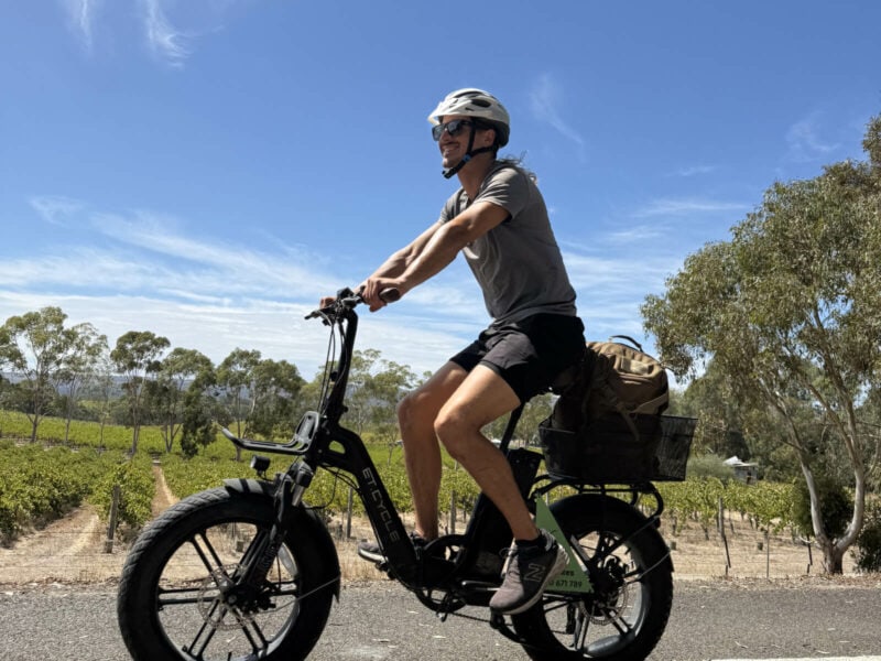 A man riding an electric bike on the Shiraz Trail, McLaren Vale, with gumtrees and rows for grape vines in the background