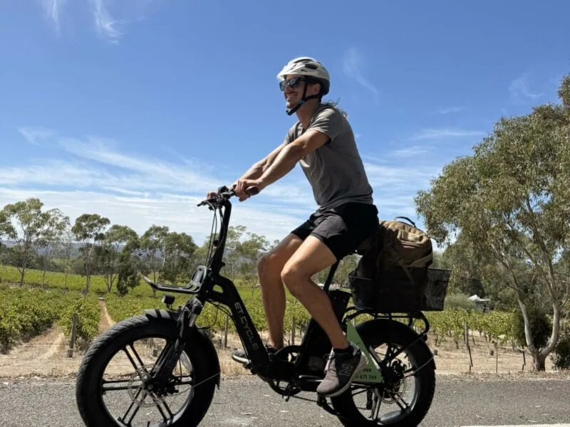 A man riding an electric bike on the Shiraz Trail, McLaren Vale, with gumtrees and rows for grape vines in the background