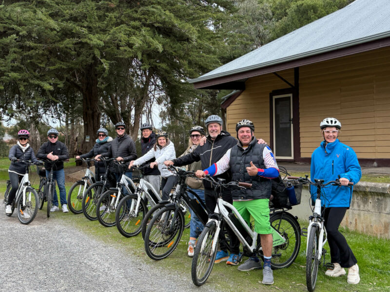 Ten adults standing next to their SA eBikes in front of the former Willunga Railway Station.