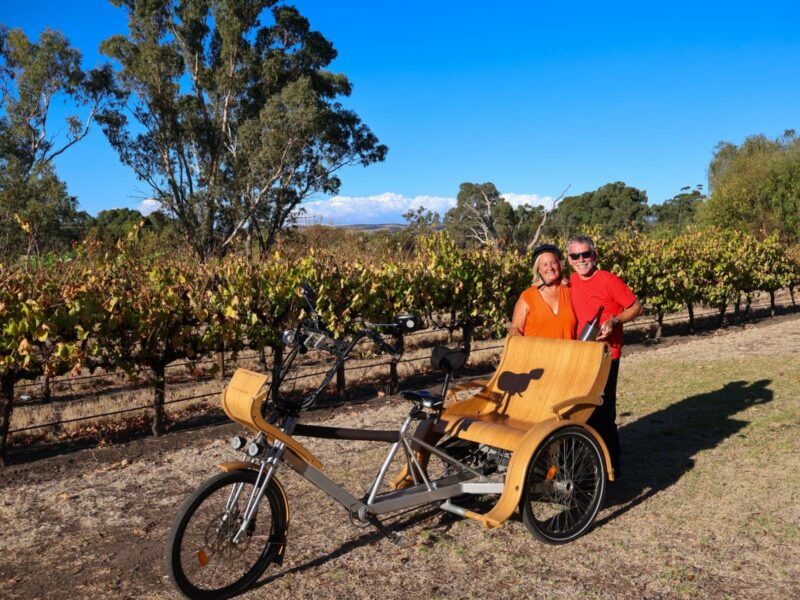 A couple standing behind a TukTuk with vines and gumtrees behind