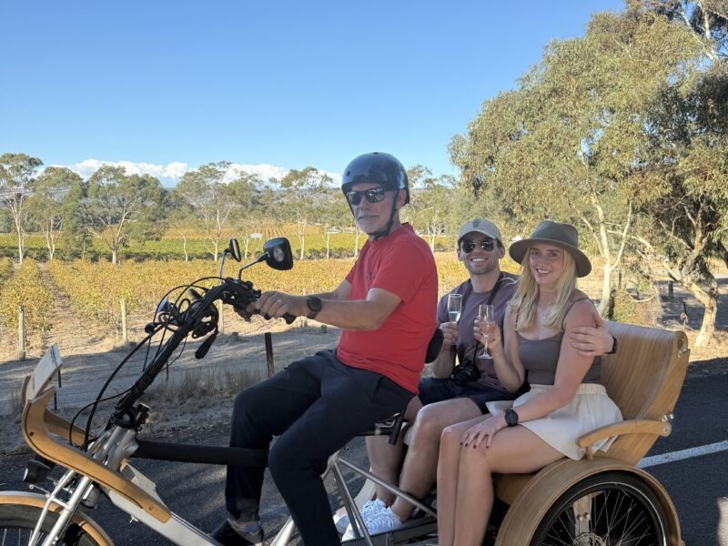 Young smiling couple sit on eTukTuk sipping champagne