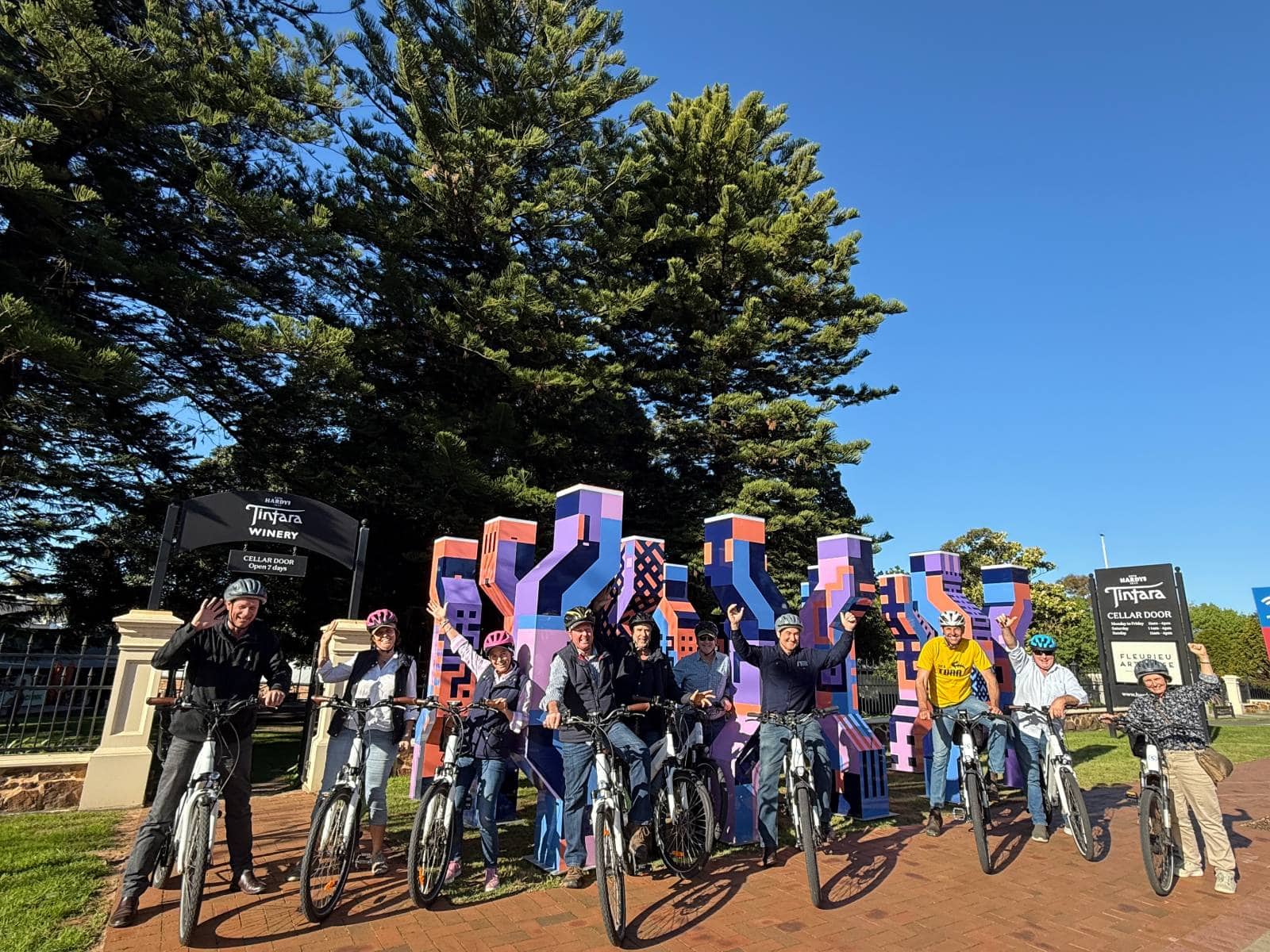 Group of riders posing in front of purple sculpture in McLaren Vale