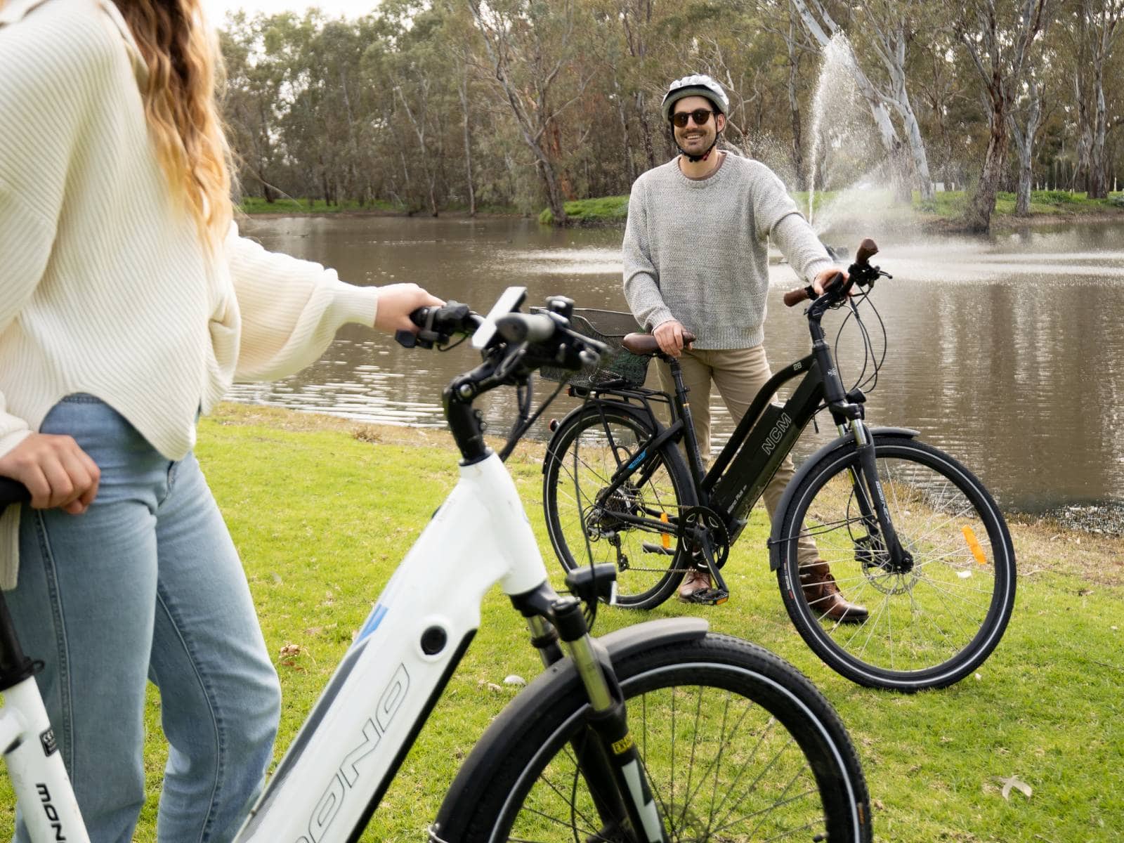 A man and a woman standing beside their e-bikes with the Serafino lake and fountain in the background