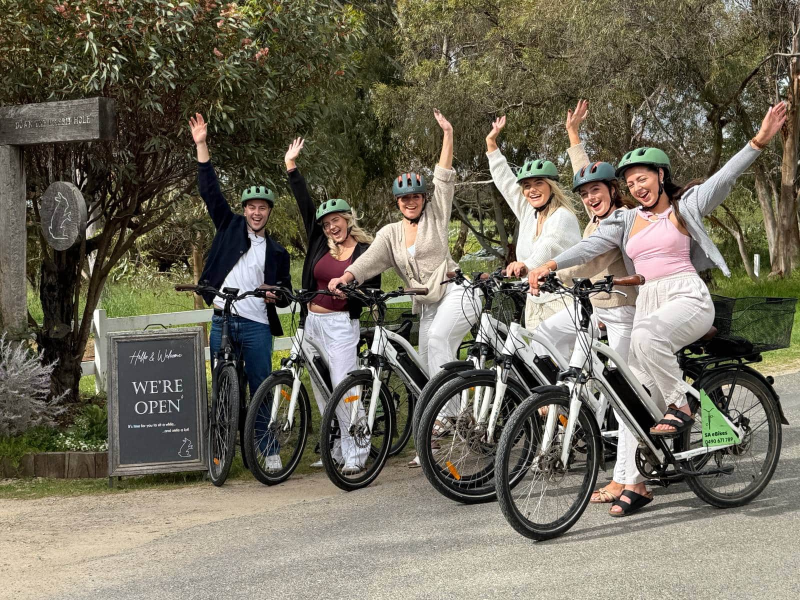 6 exhuberant young adults on their eBikes beside the sign for Down the Rabbit Hole cellar door, McLaren Vale