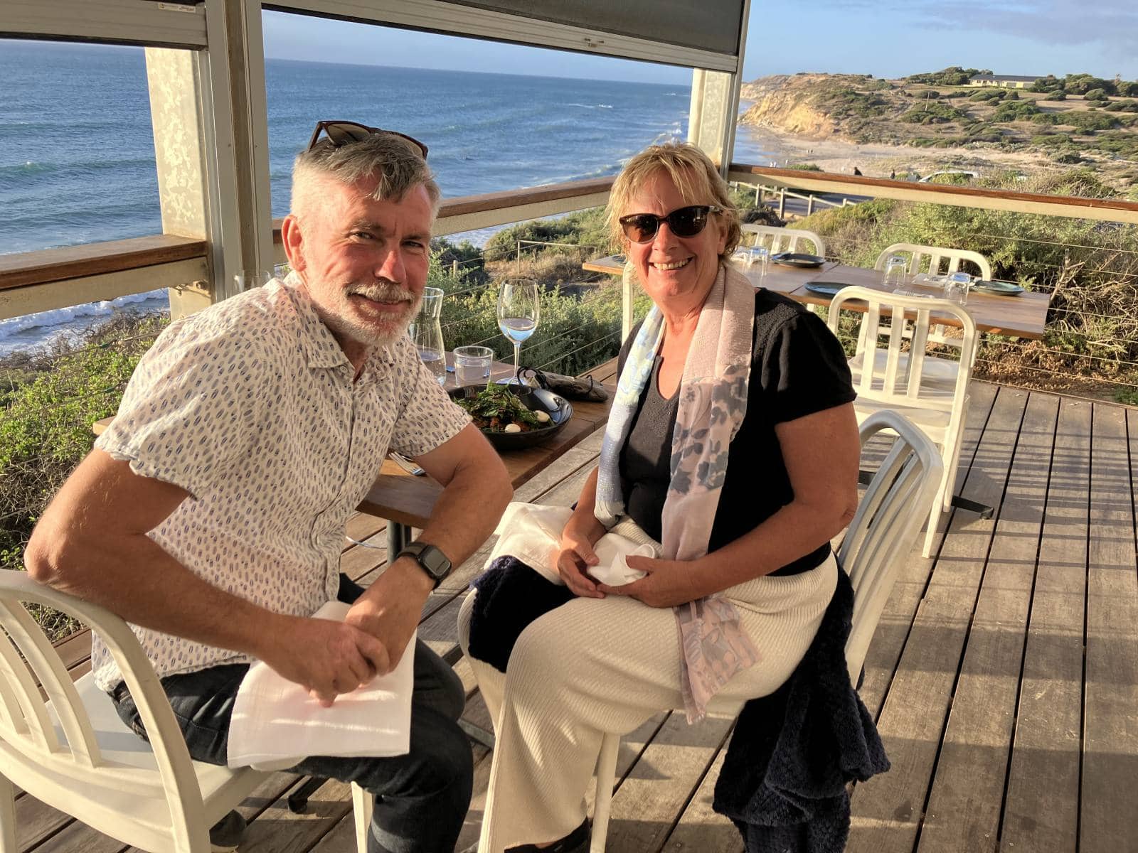 couple seated on the deck of The Star of Greece, with Port Willunga in the background