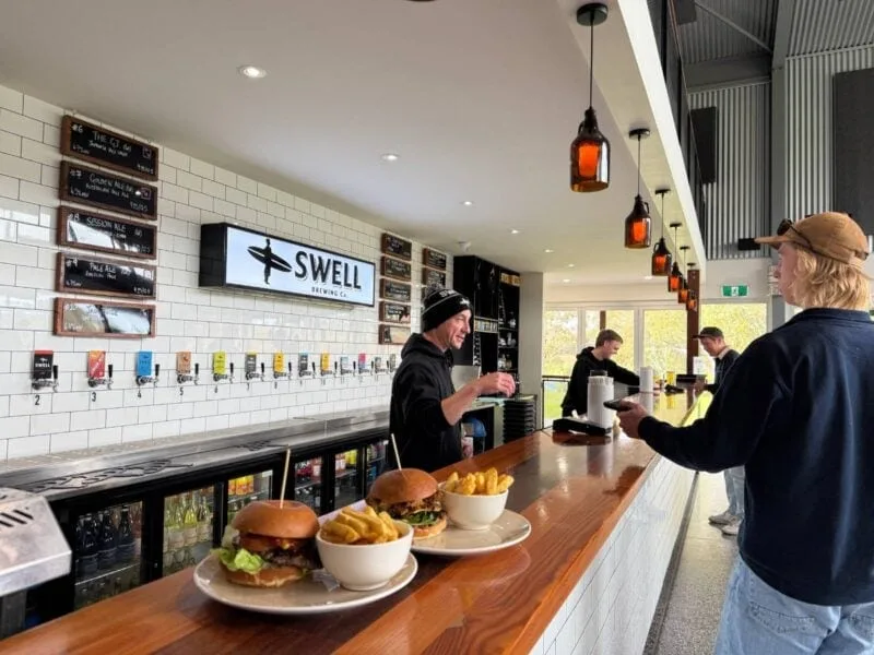 The taps and bar at Swell Brewing with 2 plates of hamburger and chips on the bar in the foreground