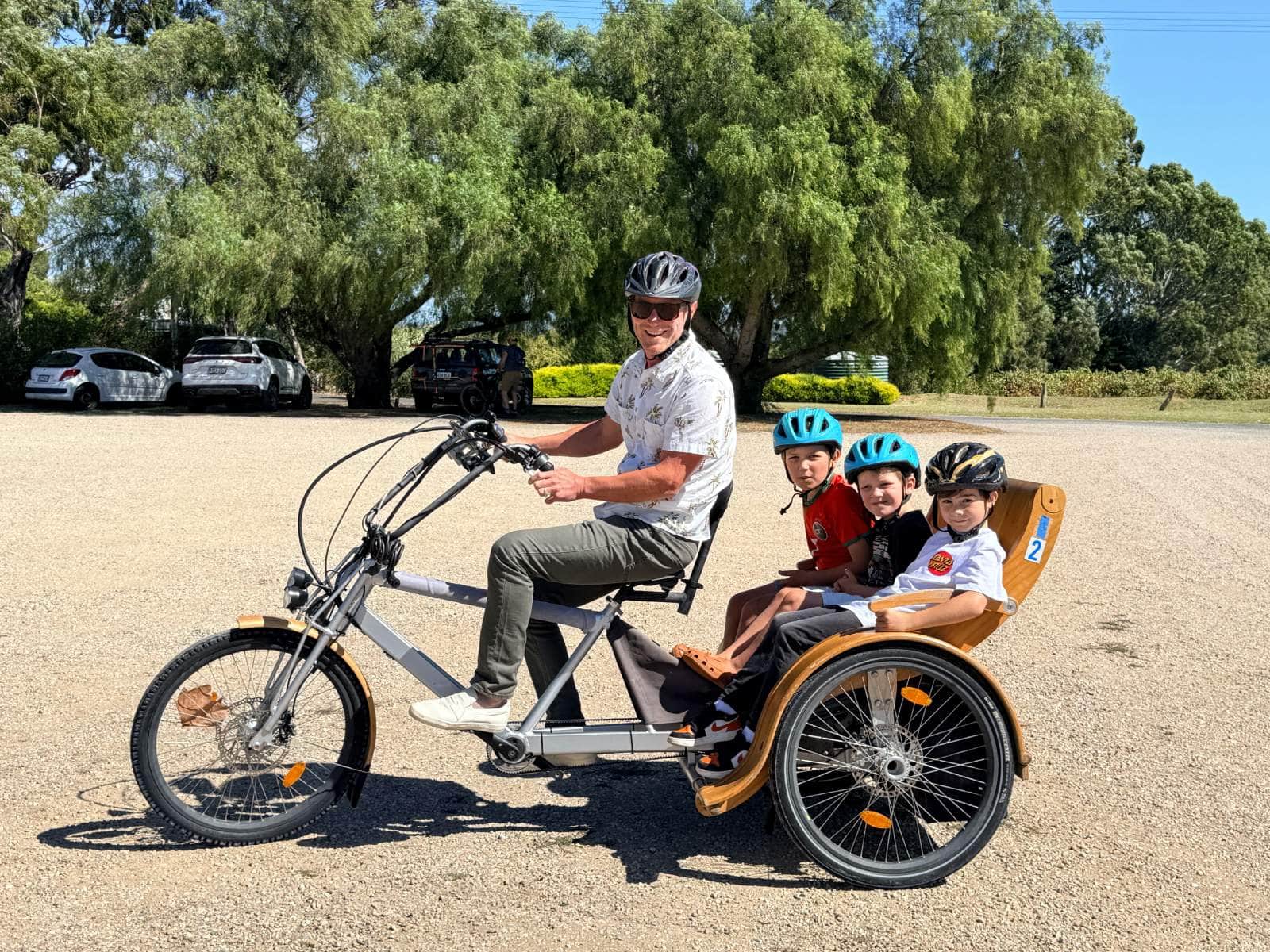 A man riding a tuktuk at Hugo Wines, with 3 children wearing helmets seated behind him.