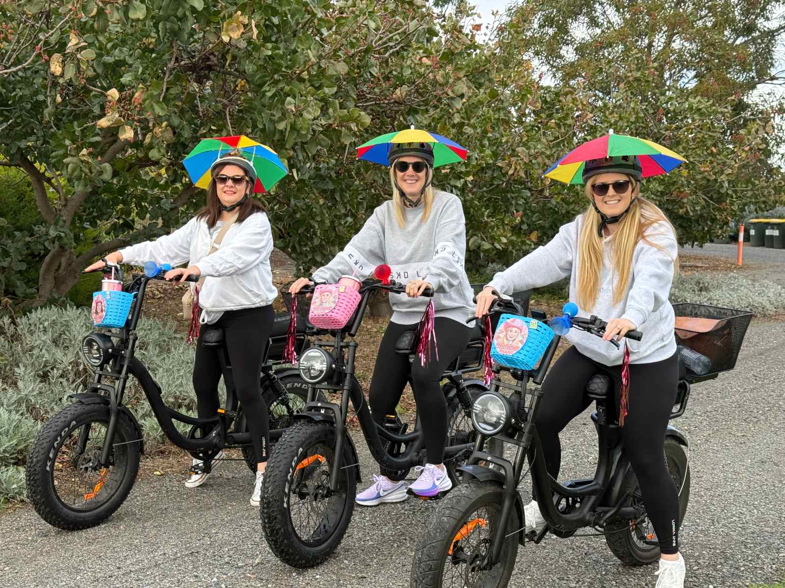 Thress women on ebikes with barbie front baskets and whimsical umbrella attachments on thier bike helmets